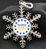 Metal snowflake ornament with 'Freedom 250' text and stars on a dark fabric background
